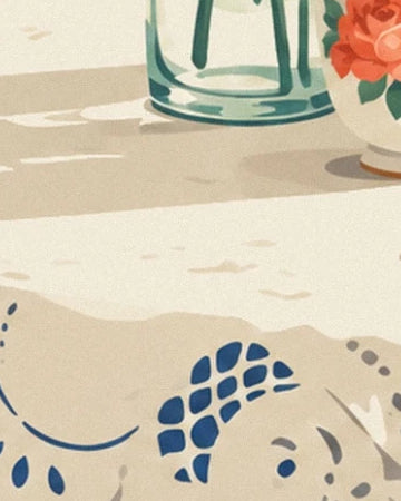 La nappe crème aux motifs bleus sous le vase en verre et son ombre allongée