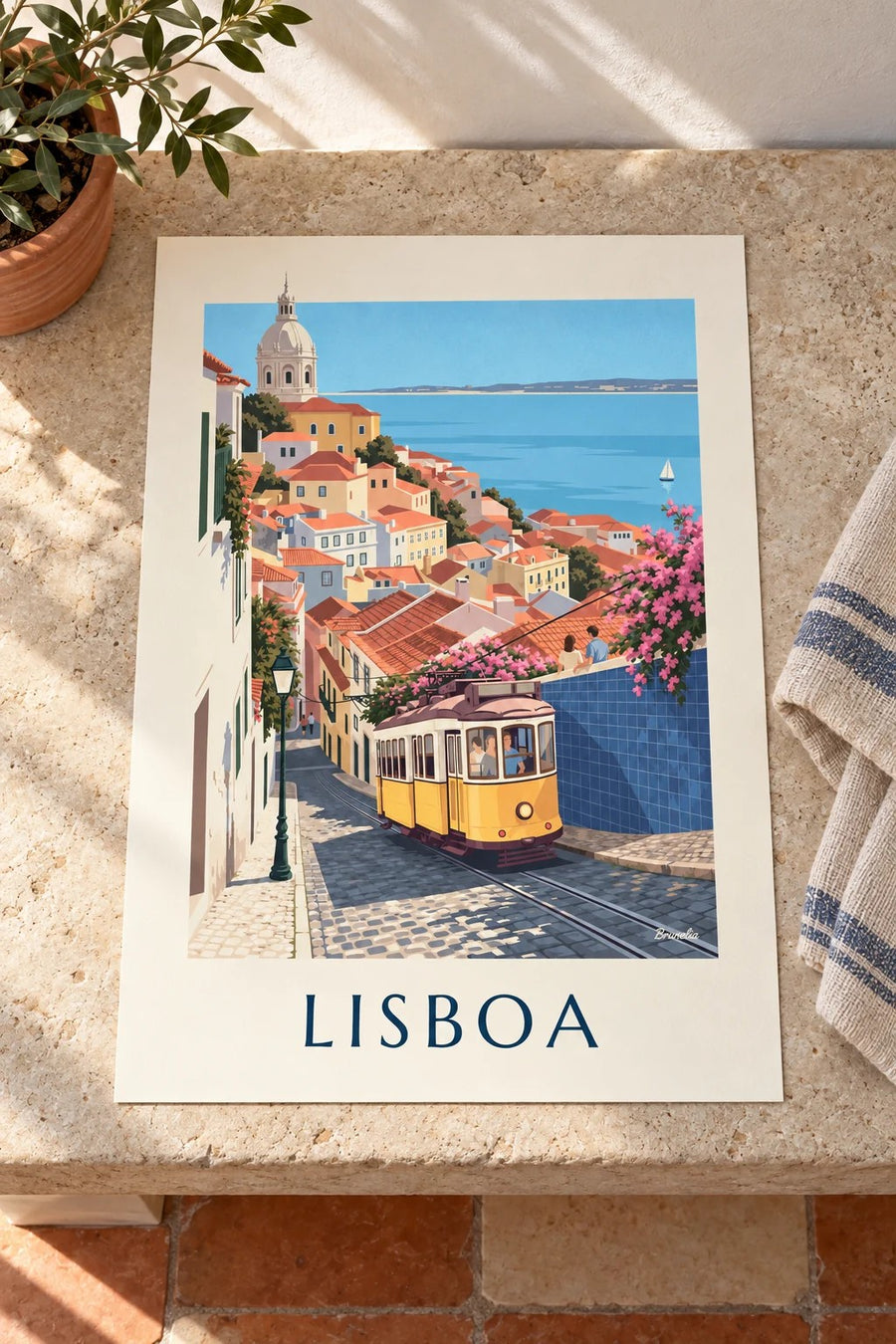 Cartaz de elétrico amarelo numa rua empedrada de Lisboa com vista para o Tejo: pousado numa mesa