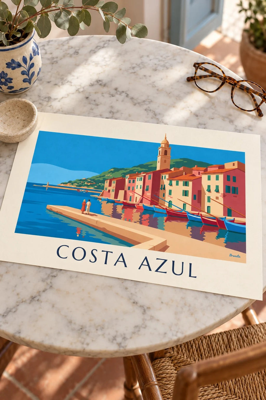 Cartaz de fachadas coloridas e barcos num porto da Côte d’Azur: pousado numa mesa